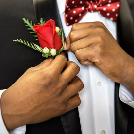 Teen pins his rose boutonniere to formal suit getting dressed and ready for prom.