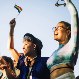Happy man and woman with hands raised holding rainbow flags while enjoying in gay pride parade