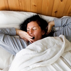 Woman with eyes closed yawning in bed at home