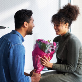 Romantic couple at home with man surprising woman with bunch of flowers celebrating valentines day, birthday or anniversary