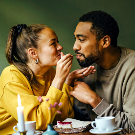 Girlfriend feeding bite of dessert to her boyfriend at cafe
