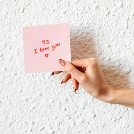 The girl holds in her hand a pink love note. Valentine's Day. White background. Woman's hand. Declaration of love. Love note. Confession note.