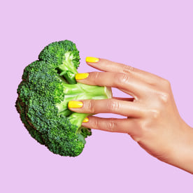 Cropped hand of woman holding broccoli against pink background