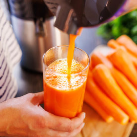 A woman pours fresh carrot juice into glass. Freshly squeezed carrot juice