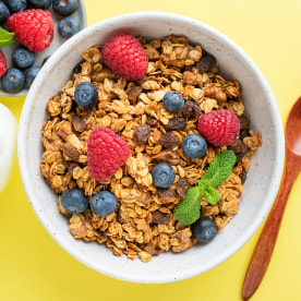 Granola with summer berries and bottle of milk on yellow background.