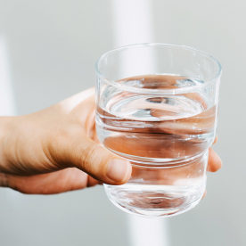 Close up of a female hand holding a glass of water against white background with sunlight. Healthy lifestyle and stay hydrated