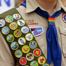 Merit badges and a rainbow-colored neckerchief slider on a Boy Scout uniform