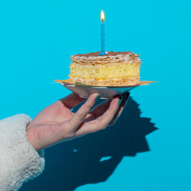 Woman's hand holding birthday cake  on plate on blue background
