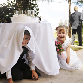 Two kids hiding underneath a table at a wedding.