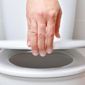 Hand of a man closing the lid of a toilet.