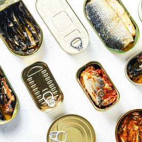 Conserves of canned fish with different types of fish and seafood, opened and closed cans with Saury, mackerel, sprats, sardines, pilchard, squid, tuna,  over white stone surface top view