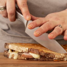 Close up of person slicing toasted sourdough cheese melt with chef's knife.