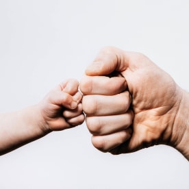 A small childs hand gives their parent a fist bump, a sign of solidarity, affection, and connection.