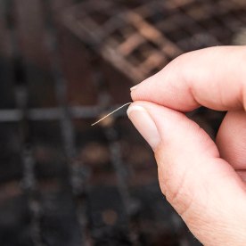 Person hand showing a loose bristle from a grill cleaning brush above a grill.