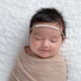 Smiling one month old baby girl swaddled in a beige wrap. Shot in the studio on a white blanket.