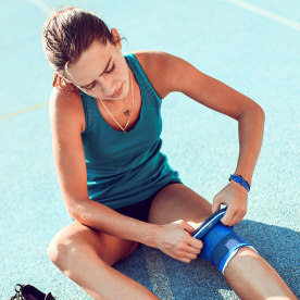 Female Bandaging Her Knee Before Running On Track.