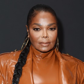 Janet Jackson stands in front of a gray background.