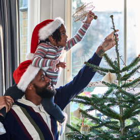 Girl on father's shoulders putting star on top of Christmas tree