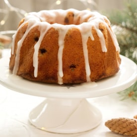 Pie with raisins and icing from powdered sugar on the background of fir branches and garlands. Rustic style.