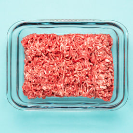 Above view of raw ground beef in a glass food container on a blue colored table.