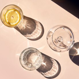 Clear glasses filled with water and refreshing drinks and lemon slices on a pastel peach colored table.