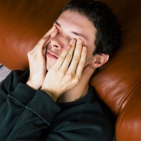 High angle view of man rubbing eyes while reclining on sofa at home.