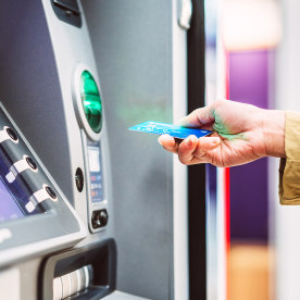 Female hand inserting bank card into automatic cash machine.