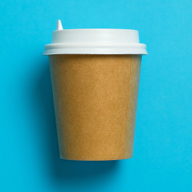 Disposable paper cup with lid for coffee on a bright pastel blue background.