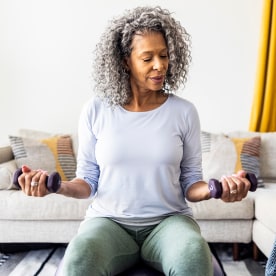 Senior woman lifting weights in living room.