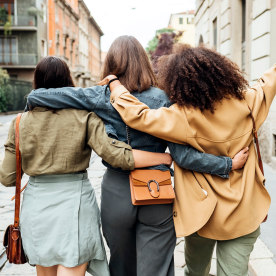 Three woman walking in the city with arm around each other.