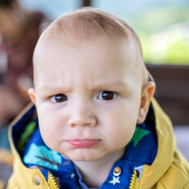 Close-up of adorable, funny little boy, in yellow jacket, with blond hair and brown eyes.