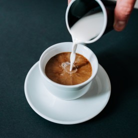 Pouring creme in cup of coffee. Close-up.