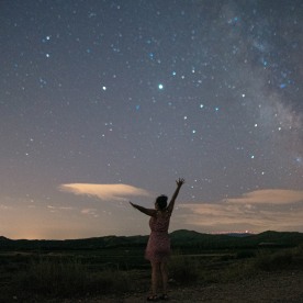 Woman with arms raised by a starry sky with a visible Milky Way