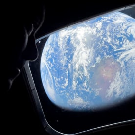Image: Close up of an astronaut looking out of a spacecraft window with a view of Earth