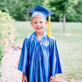 Portrait of happy boy in graduation gown standing at park