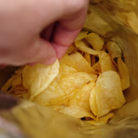 The girl takes crispy fried fatty potato chips from a package or pack. Chips in the hands of a woman, she eats them. The concept of an unhealthy diet and lifestyle, the accumulation of excess weight.