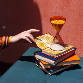 Hand reaching for a book on a stack with an hourglass on a table