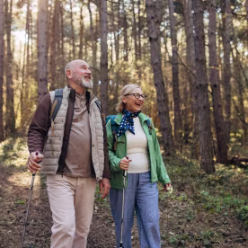 Older couple hiking in a sunlit landscape, equipped with trekking poles and backpacks, enjoying a calm and active lifestyle