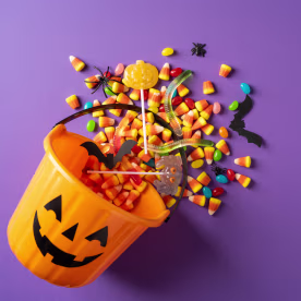 Happy Halloween jack-o'-lantern bucket spilling candy and spooky treats on purple background