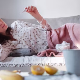 Young woman checking her temperature while lying on the couch at home