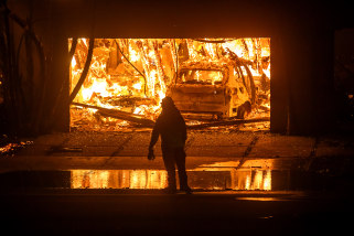 A firefighter observes a burning garage and car.