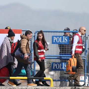 Image: Migrants are escorted by Turkish police and local officials as they arrive by ferry at the Dikili harbour in Izmir