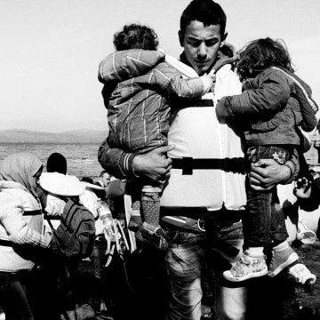 A father carries his two children from the boat after landing in Lesvos on Oct. 26.