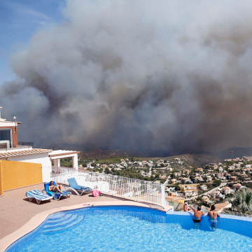Image: Two men look at a wildfire from a swimming pool as it burns nearby Benitachel village, eastern Spain
