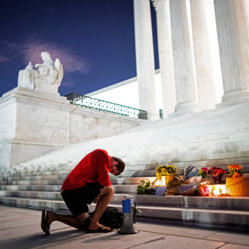 Image: A man kneels as he brings a megaphone to a vigil on the steps of the U.S. Supreme Court following the death of U.S. Supreme Court Justice Ruth Bader Ginsburg, in Washington