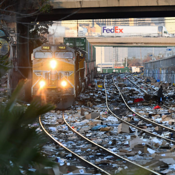 A person carries items collected from the train tracks as a Union Pacific locomotive passes through a section of Union Pacific train tracks littered with thousands of opened boxes and packages stolen from cargo shipping containers, targeted by thieves as