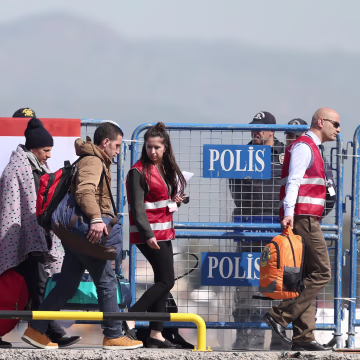 Image: Migrants are escorted by Turkish police and local officials as they arrive by ferry at the Dikili harbour in Izmir