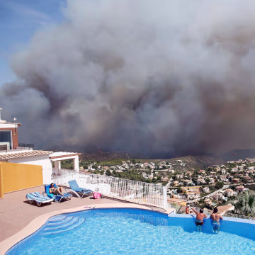 Image: Two men look at a wildfire from a swimming pool as it burns nearby Benitachel village, eastern Spain
