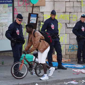 Image: A migrant rides his bike past French police