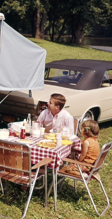 1960s FAMILY WITH THREE DAUGHTERS AT TABLE BY AUTOMOBILE AND TRAILER FIVE EATING FOOD VACATION MAN WOMAN GIRL. H. ARMSTRONG ROBERTS/CLASSICSTOCK/Everett Collection (kc3535)